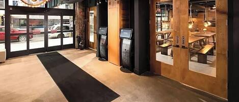 A modern interior with a reception area, wooden walls, and a black carpet leading to a seating area with tables and chairs.