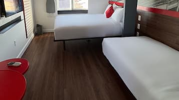A room with two beds, a red table, a window, and a wall-mounted ironing board.
