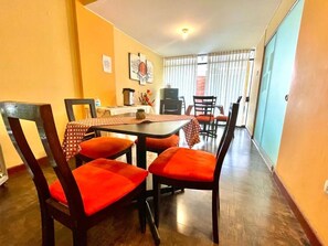 A dining area with a table and chairs, a television, and a window with curtains.