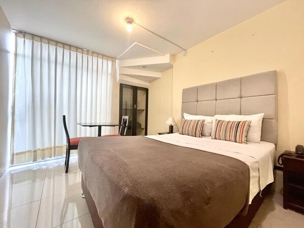 A hotel room with a large bed, a chair, a table, and a window with curtains.