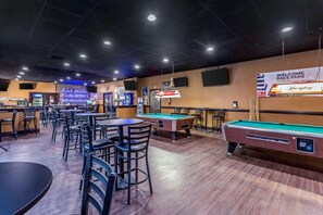 Una sala de billar con mesas de pool, sillas, una zona de bar y una pantalla de televisión.
