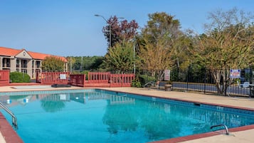Una piscina con valla roja, un cartel de advertencia de socorrista y un edificio con tejado rojo al fondo.