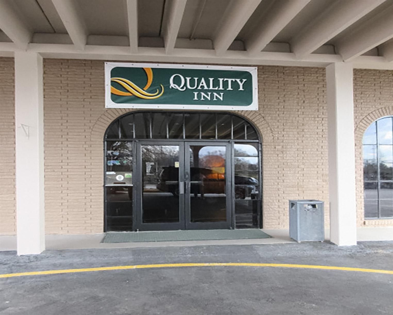 The exterior of a Quality Inn hotel with a brick facade, a large arched entrance, and a sign above the doors.