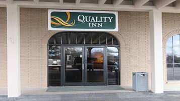 The exterior of a Quality Inn hotel with a brick facade, a large arched entrance, and a sign above the doors.