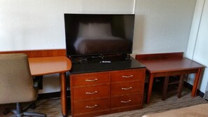 Habitación de hotel con televisor sobre un mueble de madera, una mesita pequeña de madera y una silla.