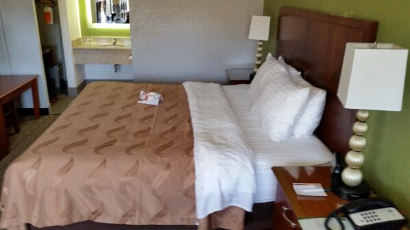 Una habitación de hotel con cama, mesita de noche, lámpara y un pequeño escritorio con teléfono.
