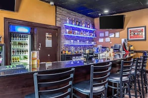 Zona de bar con barra, taburetes y estantes llenos de botellas.