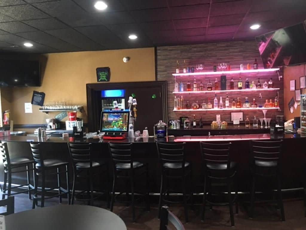 A bar area with multiple seating options, a counter with a variety of bottles, and a television screen.