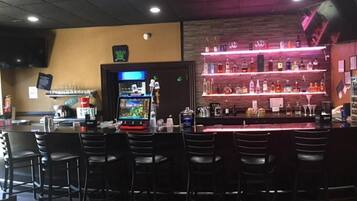 A bar area with multiple seating options, a counter with a variety of bottles, and a television screen.