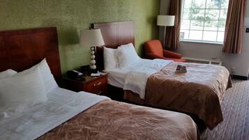 Habitación de hotel con dos camas, una mesita de noche con lámpara, una silla y una ventana con cortinas.