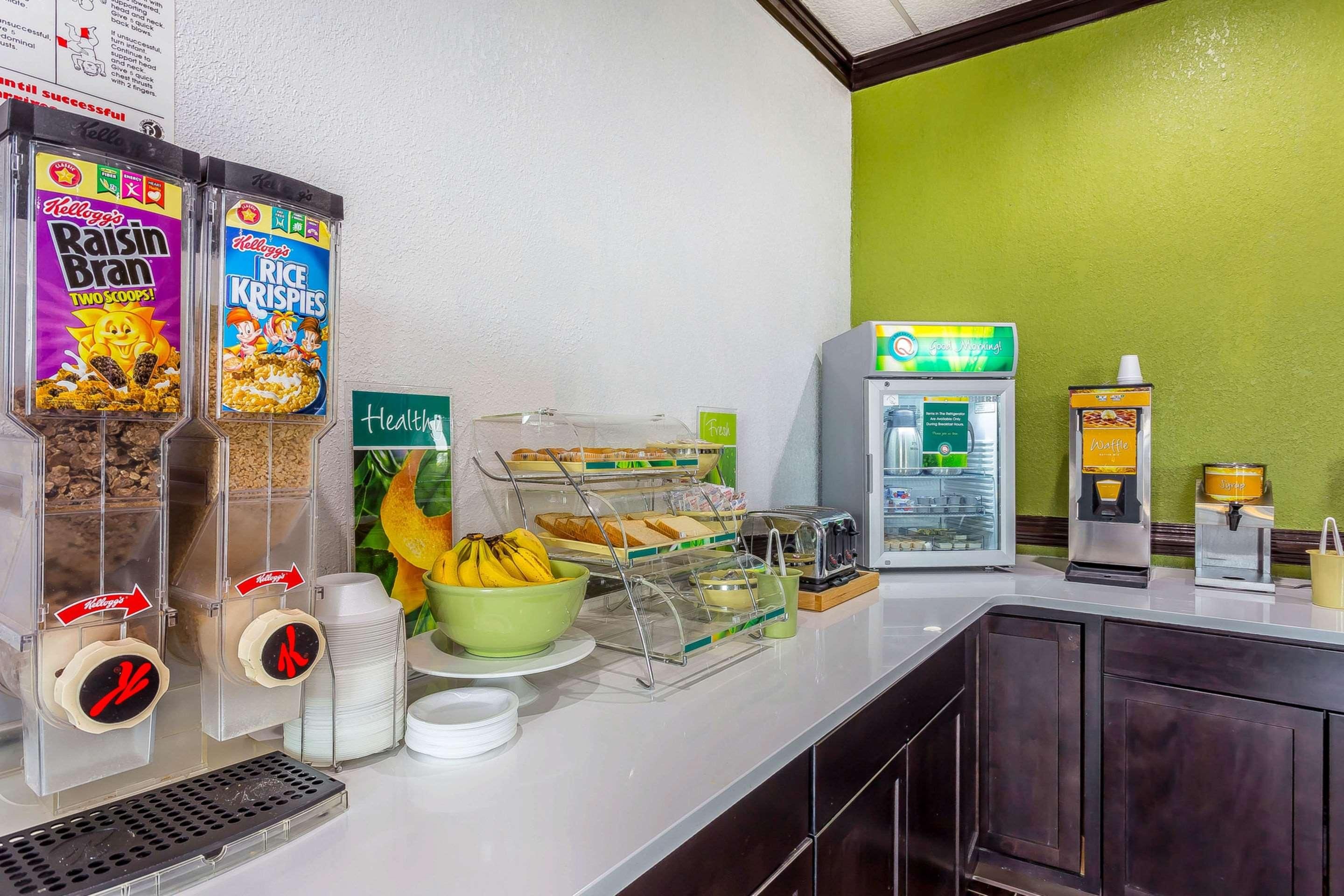 Una barra de desayuno con cereales, una máquina de café, un dispensador de zumo y un tostador.