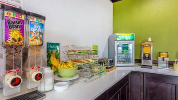 Una barra de desayuno con cereales, una máquina de café, un dispensador de zumo y un tostador.
