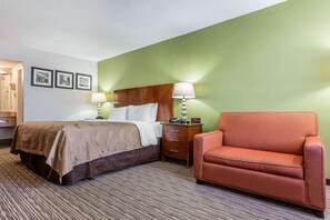 Una habitación de hotel con una cama, una mesita de noche, una silla y una pared con cuadros enmarcados.