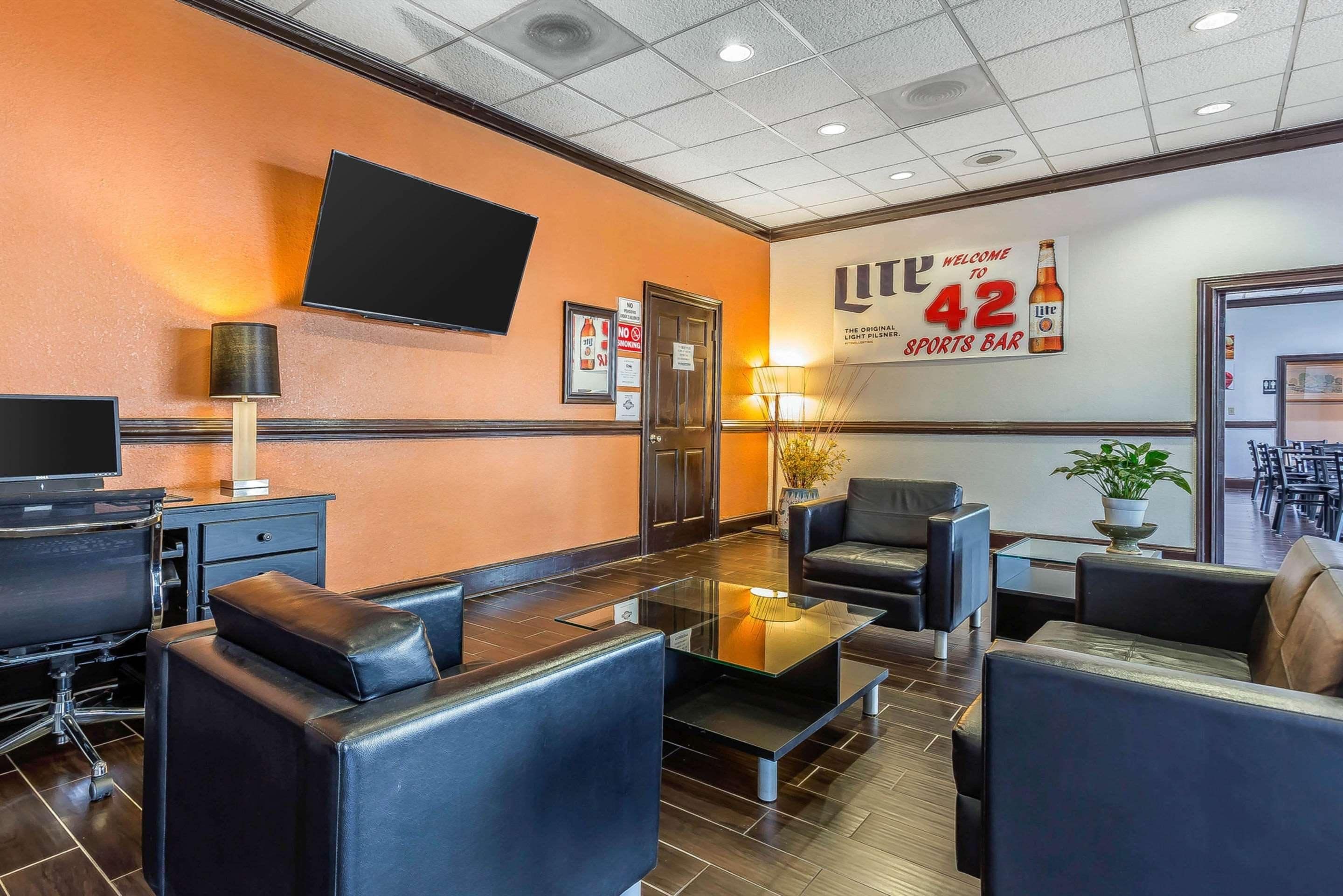 A hotel lobby with leather seating, a flat-screen TV, and a wall sign advertising a sports bar.