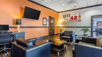 A hotel lobby with leather seating, a flat-screen TV, and a wall sign advertising a sports bar.