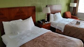A hotel room with two beds, a nightstand with a lamp, and a chair.