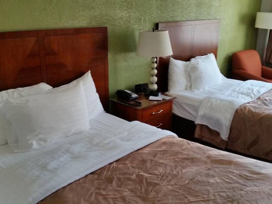 A hotel room with two beds, a nightstand with a lamp, and a chair.