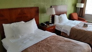 Habitación de hotel con dos camas, una mesita de noche con lámpara y una silla.