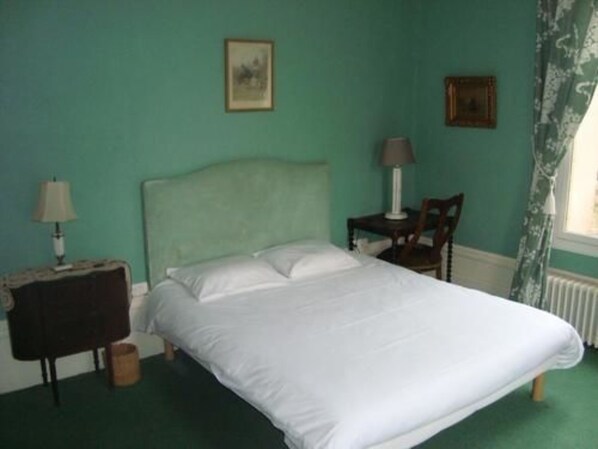 Un dormitorio con cama, mesita de noche, una silla y dos lámparas de pared.