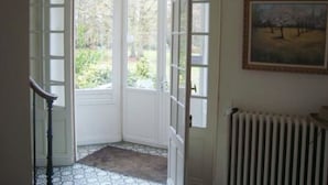 Een kamer met een grote witte deur die uitkomt op een tuin, een radiator en een lijst met een schilderij aan de muur.
