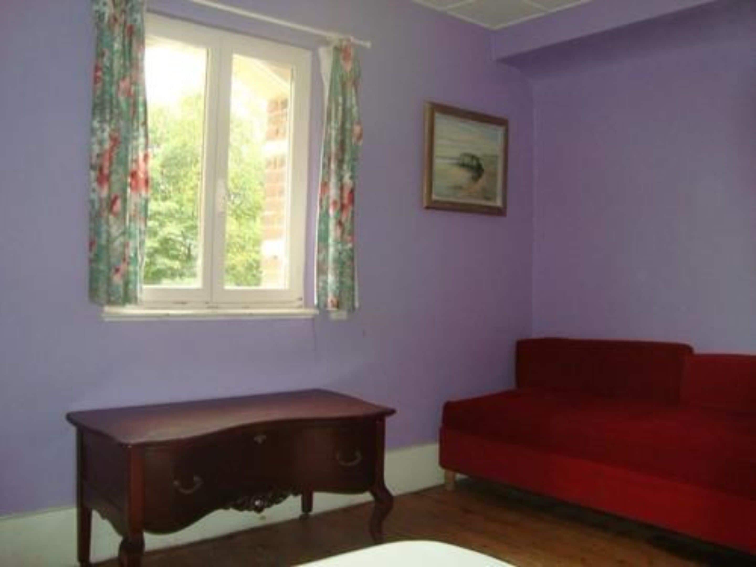 Una habitación con ventana, un sofá rojo y un armario de madera.