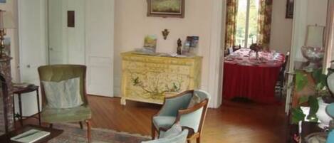A room with a wooden floor, a yellow dresser, a green armchair, a blue armchair, and a dining table with a red tablecloth.