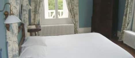 A bedroom with a bed, a nightstand, a lamp, a dresser, and a window with curtains.