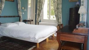 Een slaapkamer met een bed, een houten bureau, een stoel, een radiator en een raam met gordijnen.