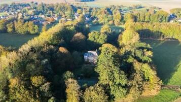A rural landscape with a large house surrounded by dense trees and fields.