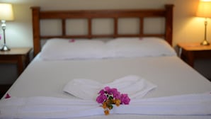 Een net opgemaakt bed met witte lakens, een houten hoofdbord en een bloemstuk op het bed.