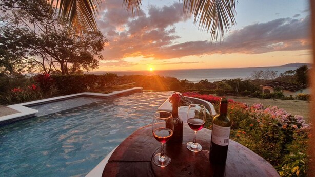 Zonsondergang uitzicht vanaf een zwembadgedeelte, met een fles wijn en glazen op een tafel.
