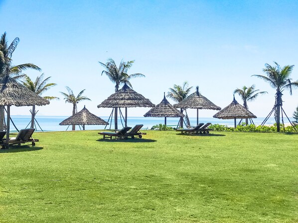 A beach with thatched umbrellas and lounge chairs.