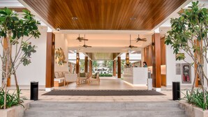 A modern hotel lobby with a wooden ceiling, a reception desk, seating area, and large windows. - The Ocean Villas (Da Nang Municipality)