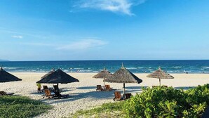 A beach with thatched umbrellas and lounge chairs at The Ocean Resort. - The Ocean Villas (Da Nang)
