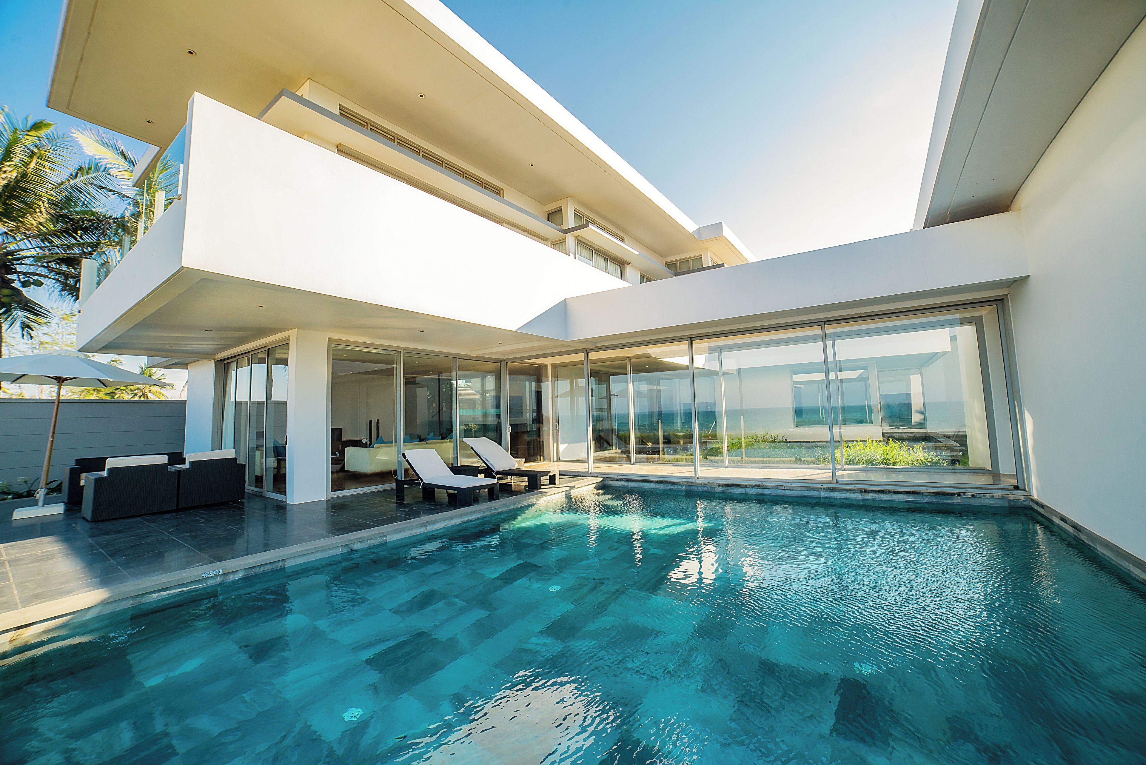 A modern pool area with clear blue water, sun loungers, and a glass-enclosed patio.
