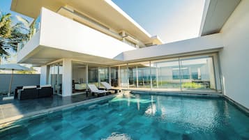 Un área de piscina moderna con agua azul cristalina, sillas de tomar el sol y un patio con paredes de vidrio.