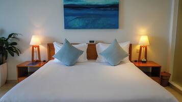 A neatly made bed with two pillows, a nightstand with a lamp, and a painting on the wall.