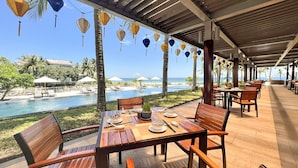 A covered outdoor dining area with tables and chairs, overlooking a pool and beach. - The Ocean Villas (Da Nang Municipality)