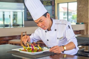 Un chef con uniforme blanco y un gorro alto, preparando un plato en un plato blanco.