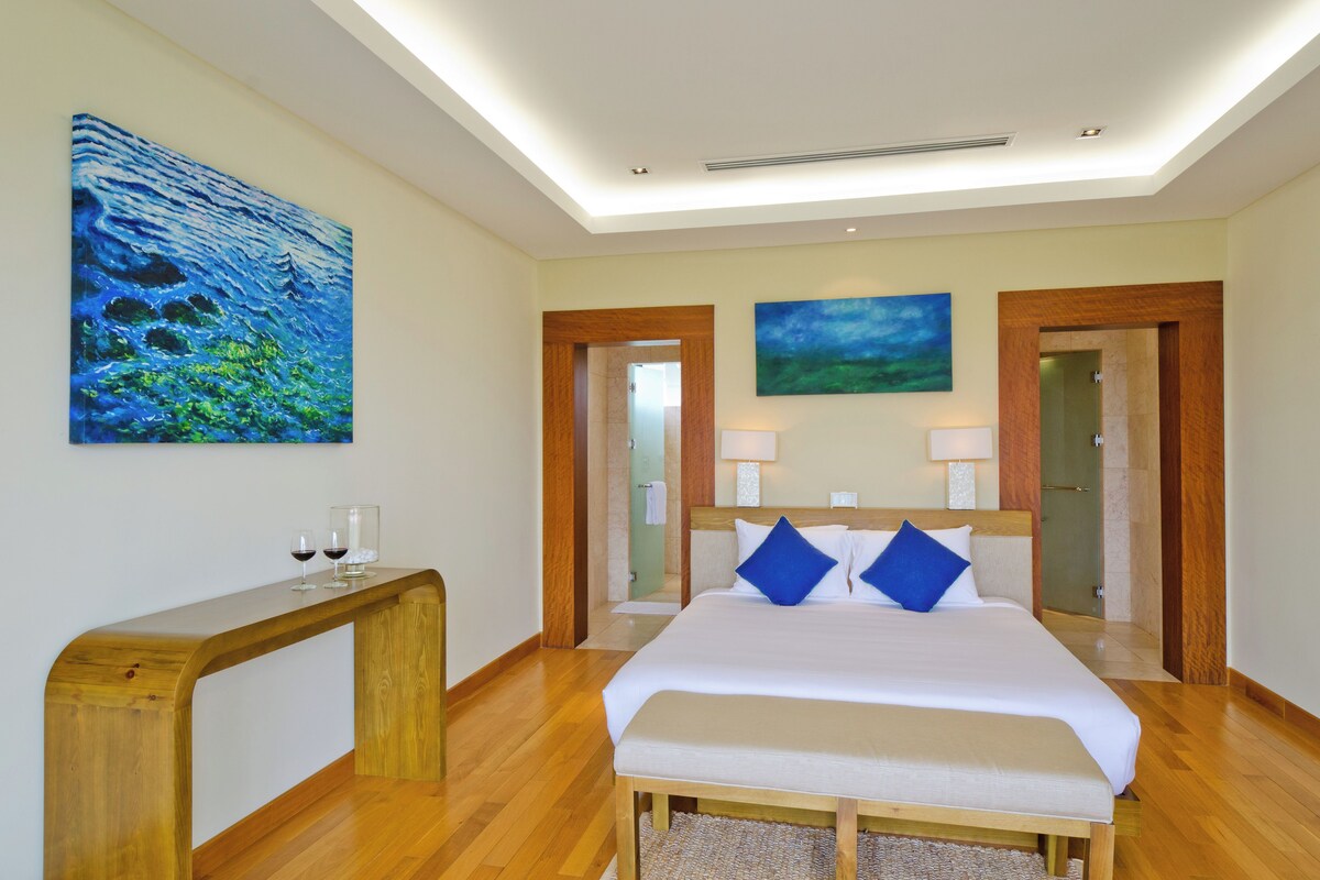 Een hotelkamer met een groot bed, twee nachtkastjes, een houten bankje en kunst aan de muren.
