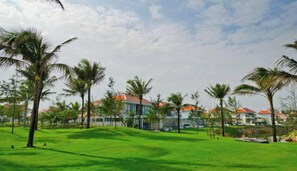 A grassy area with palm trees and buildings with red roofs in the background. - The Ocean Villas (Da Nang Municipality)