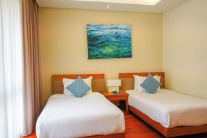 A hotel room with two beds, a nightstand, a painting on the wall, and a window with curtains. - The Ocean Villas (Da Nang Municipality)