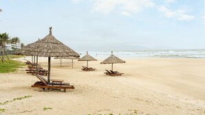 A beach with thatched umbrellas and wooden lounge chairs. - The Ocean Villas (Da Nang Municipality)