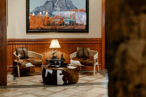 A lobby with two leather armchairs, a wooden coffee table, and a framed landscape painting on the wall.