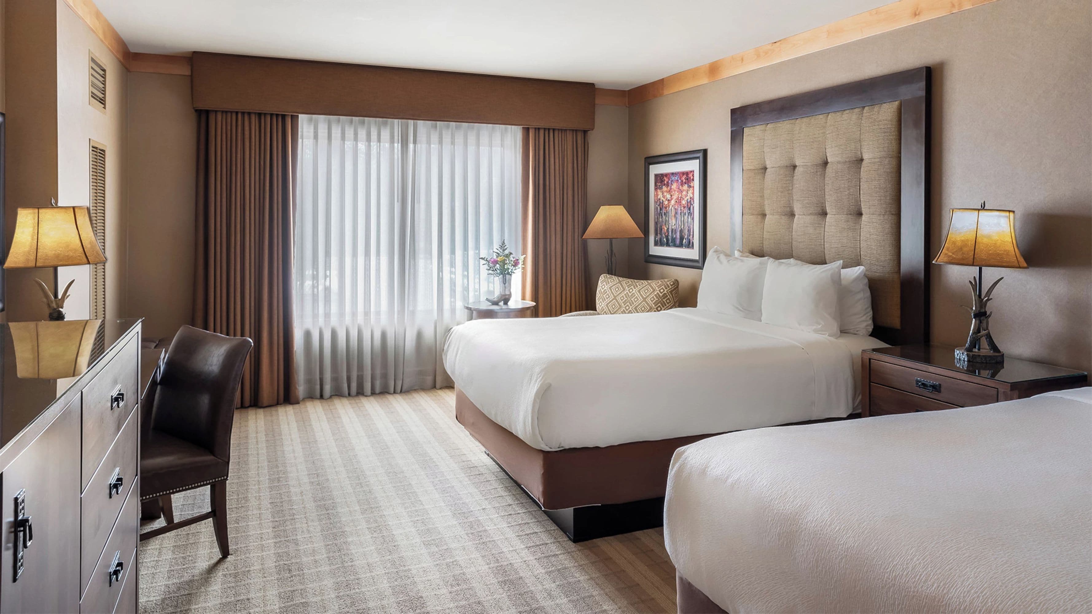 A hotel room with a large bed, a smaller bed, a desk, a chair, and a dresser.