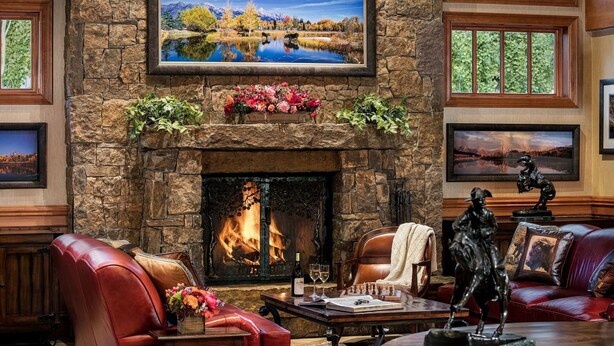 A fireplace with a stone mantle, a red leather sofa, and a table with a statue. - Wyoming Inn of Jackson Hole (Jackson)