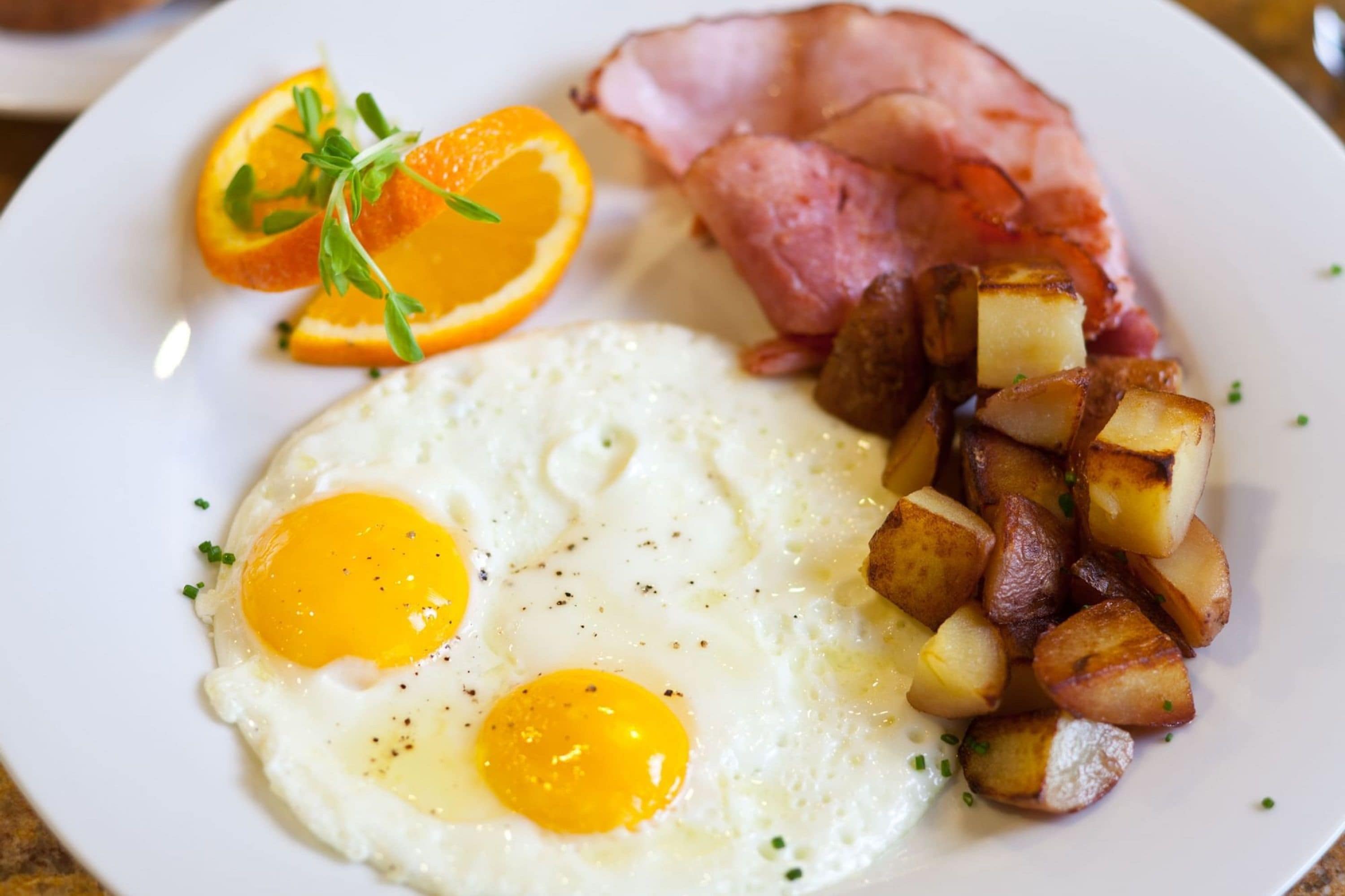 A plate with fried eggs, roasted potatoes, bacon, and an orange slice.