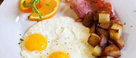 A plate with fried eggs, roasted potatoes, bacon, and an orange slice.