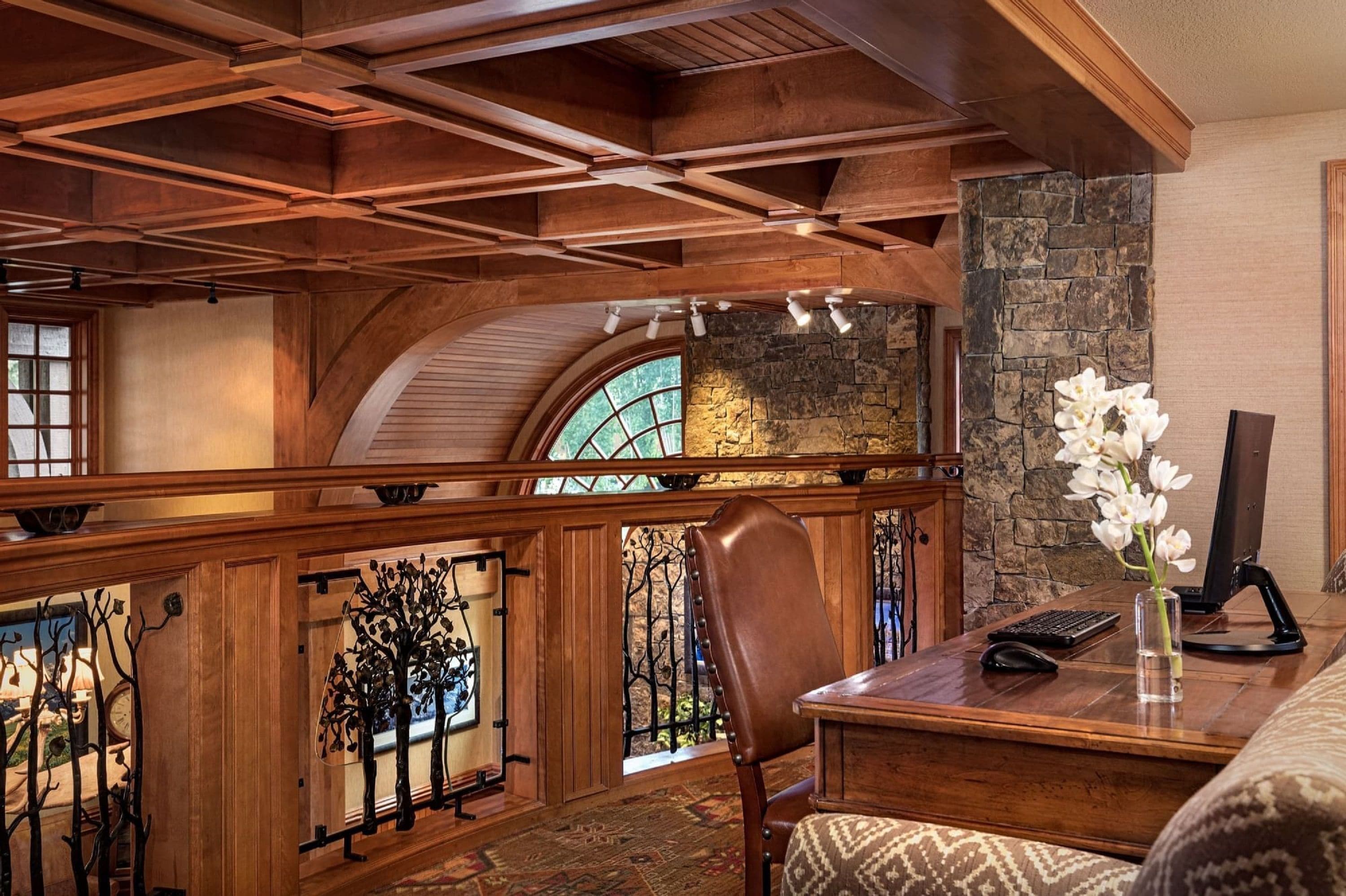 A wooden interior with a stone fireplace, a desk with a computer, and a chair.