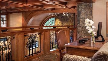 A wooden interior with a stone fireplace, a desk with a computer, and a chair.